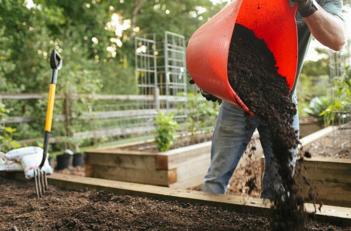 person adding compost to a garden bed to prepare healthy soil